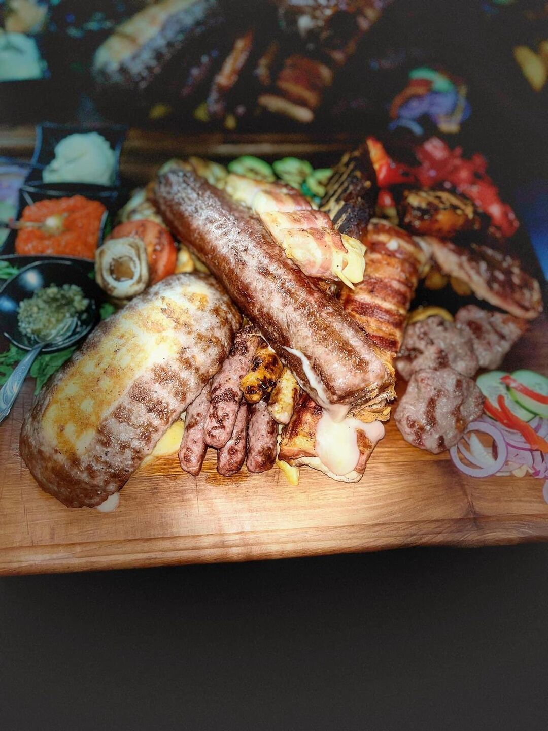 Daska s miješanim mesom: punjena pljeskavica, kobasica, ćevapi i meso omotano slaninom, uz umake
