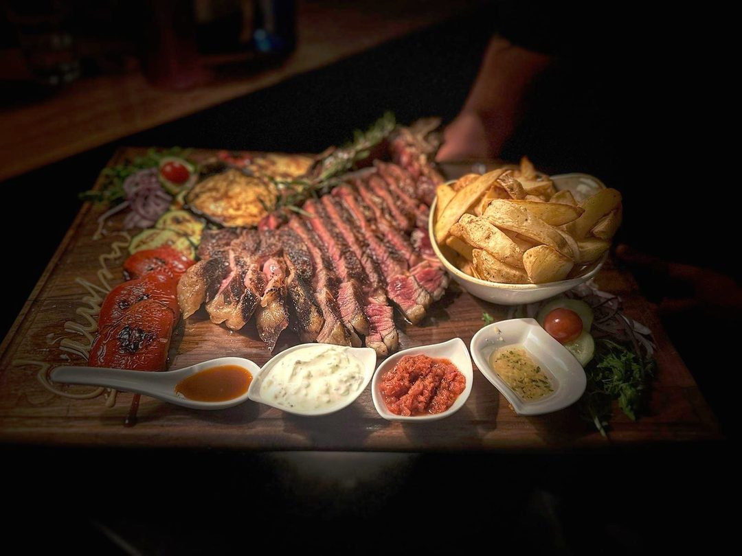 Narezani T-bone odrezak na dasci s povrćem s roštilja, krumpirom i četiri umaka