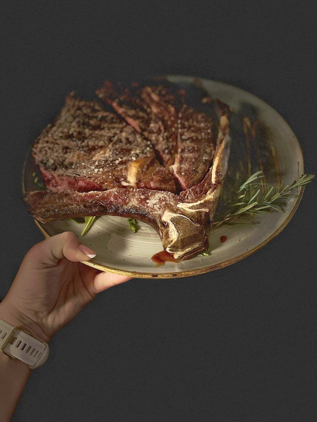 Ruka drži tanjur s T-bone odreskom i ružmarinom