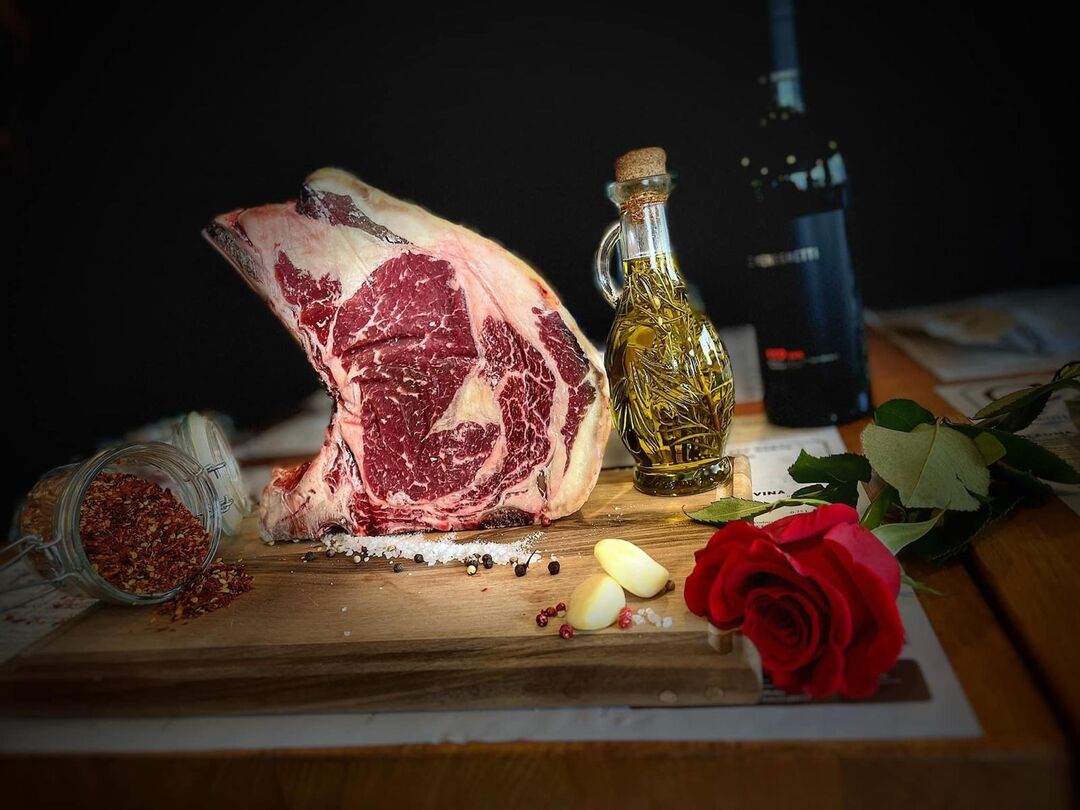 Sirovi goveđi odrezak s kosti na dasci, uz ulje s ružmarinom, češnjak, papar, vino i crvenu ružu